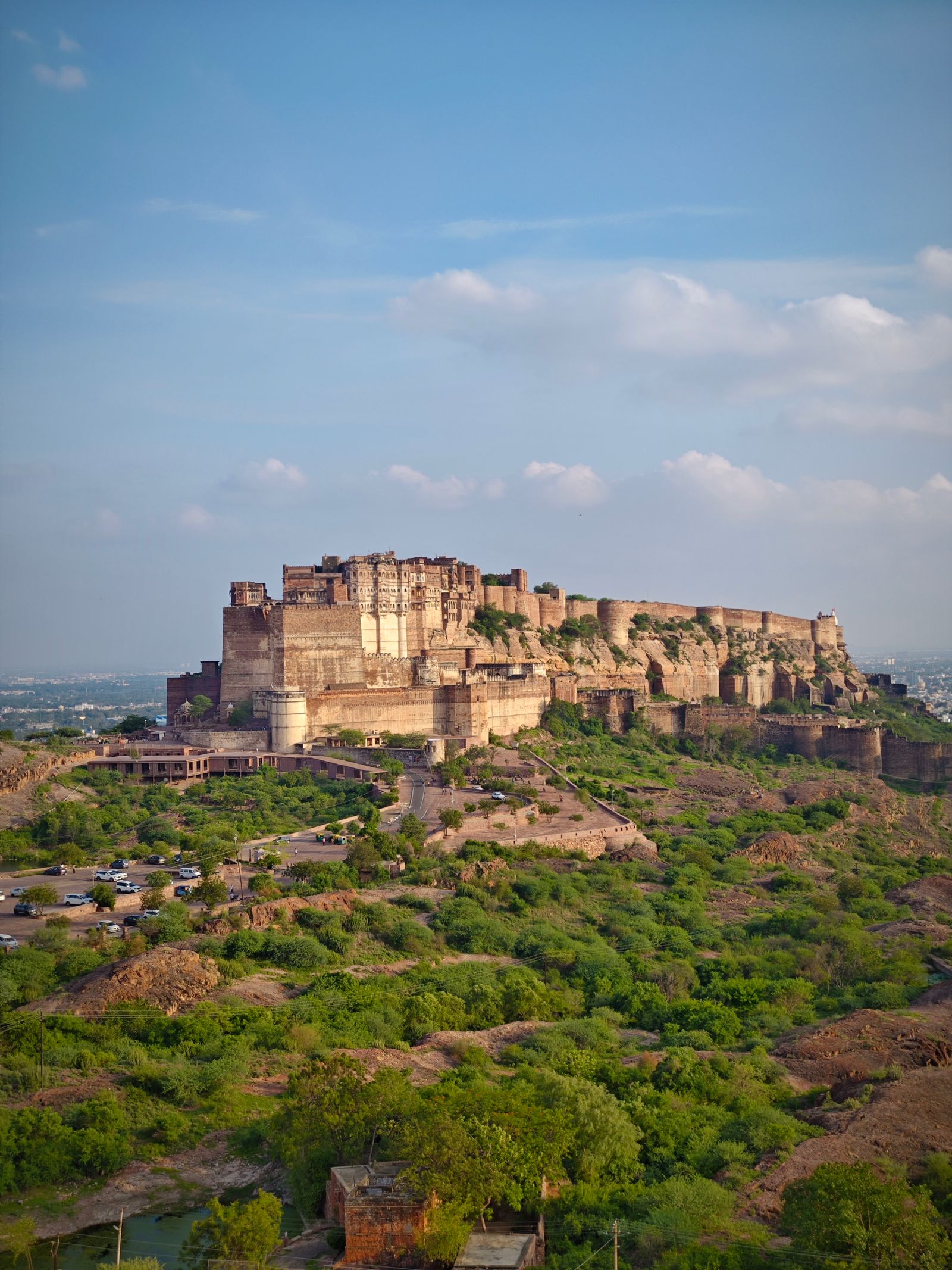 Mehrangarh Fort rising above green seasonal vegetation beneath a blue sky